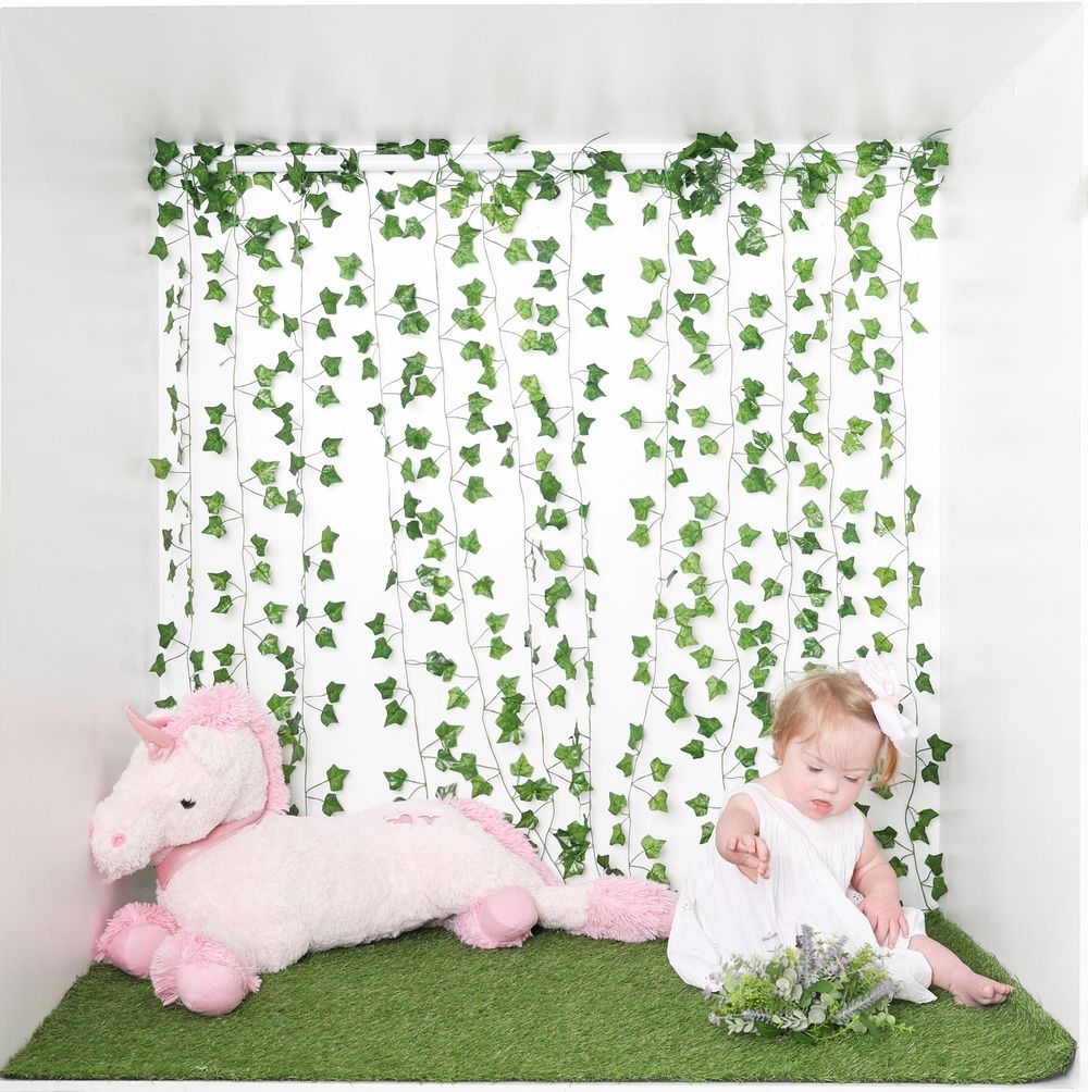 Baby in pink tutu dress lying on grass mat with leafy green vine backdrop creates dreamy photo setup.