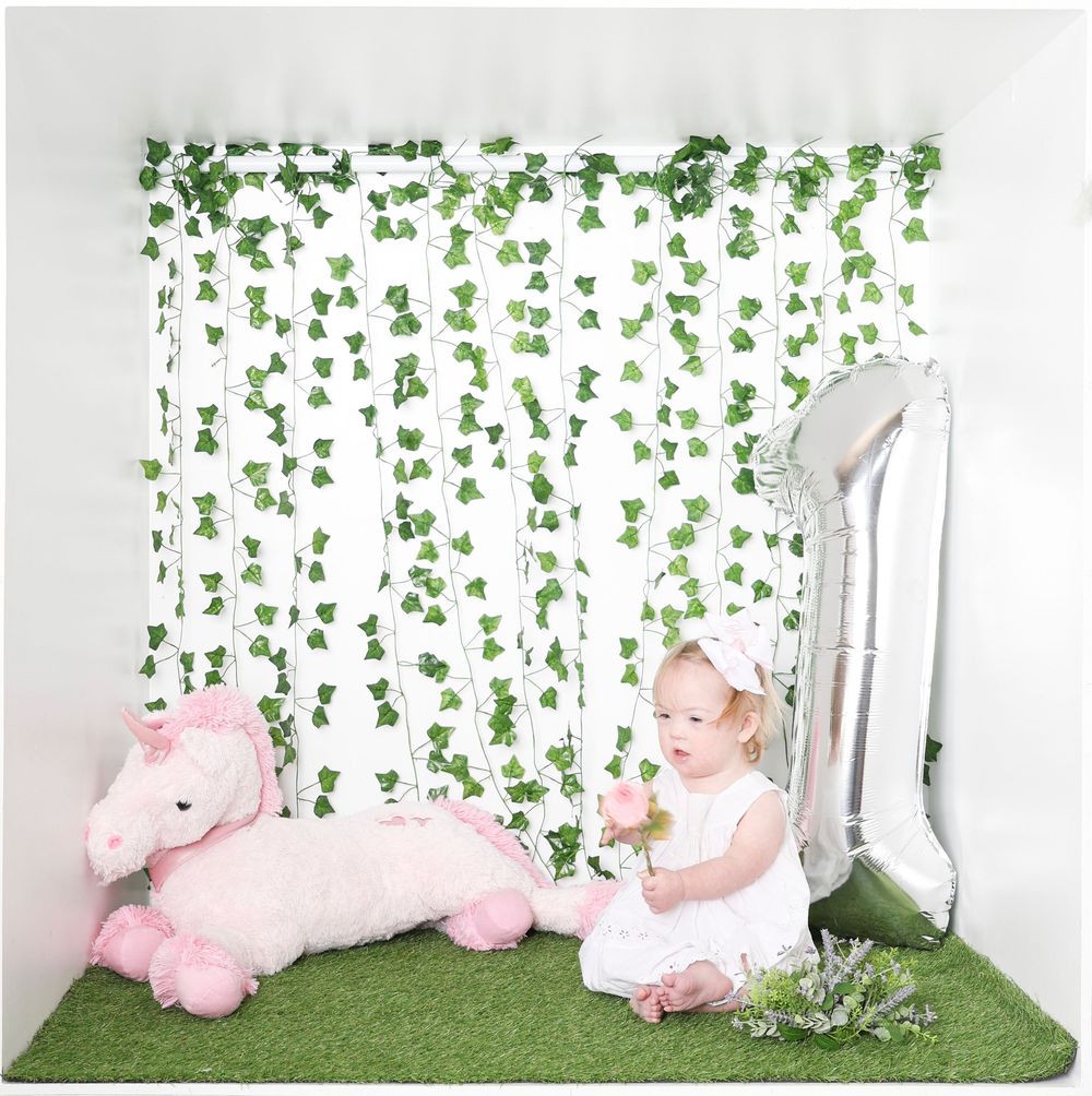 Sweet photo setup with pink tulle decorations, greenery backdrop, and white furniture for a whimsical garden theme.