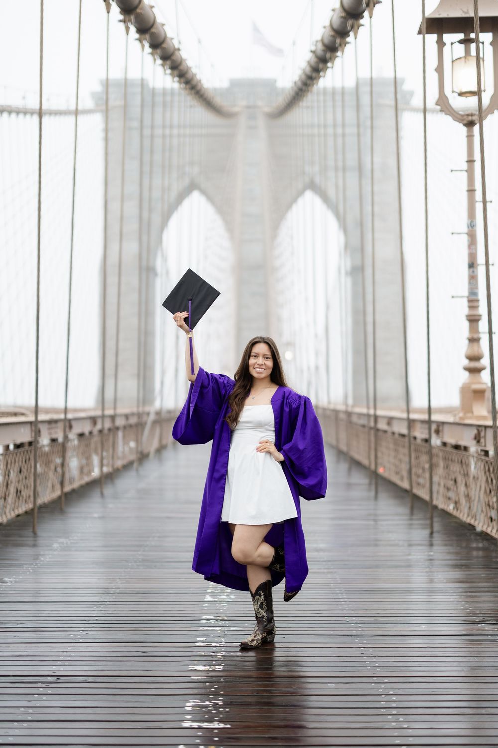 A graduation photoshoot on the Brooklyn Bridge featuring someone in a purple academic robe throwing their cap.