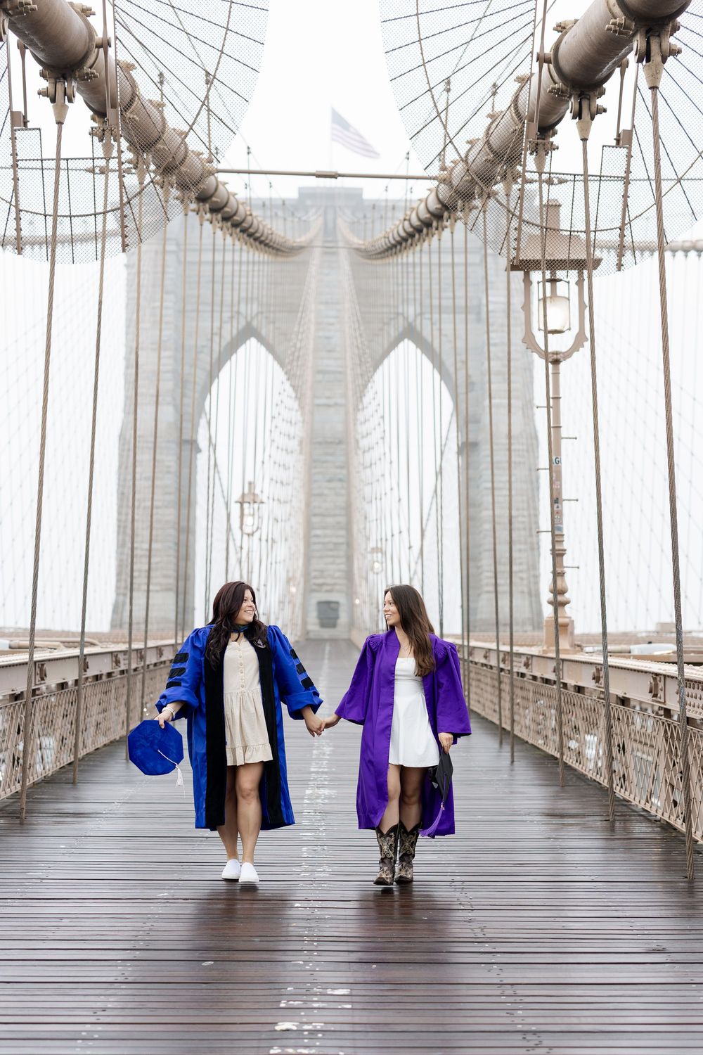 People in blue and purple coats walking along the wooden planks of Brooklyn Bridge.