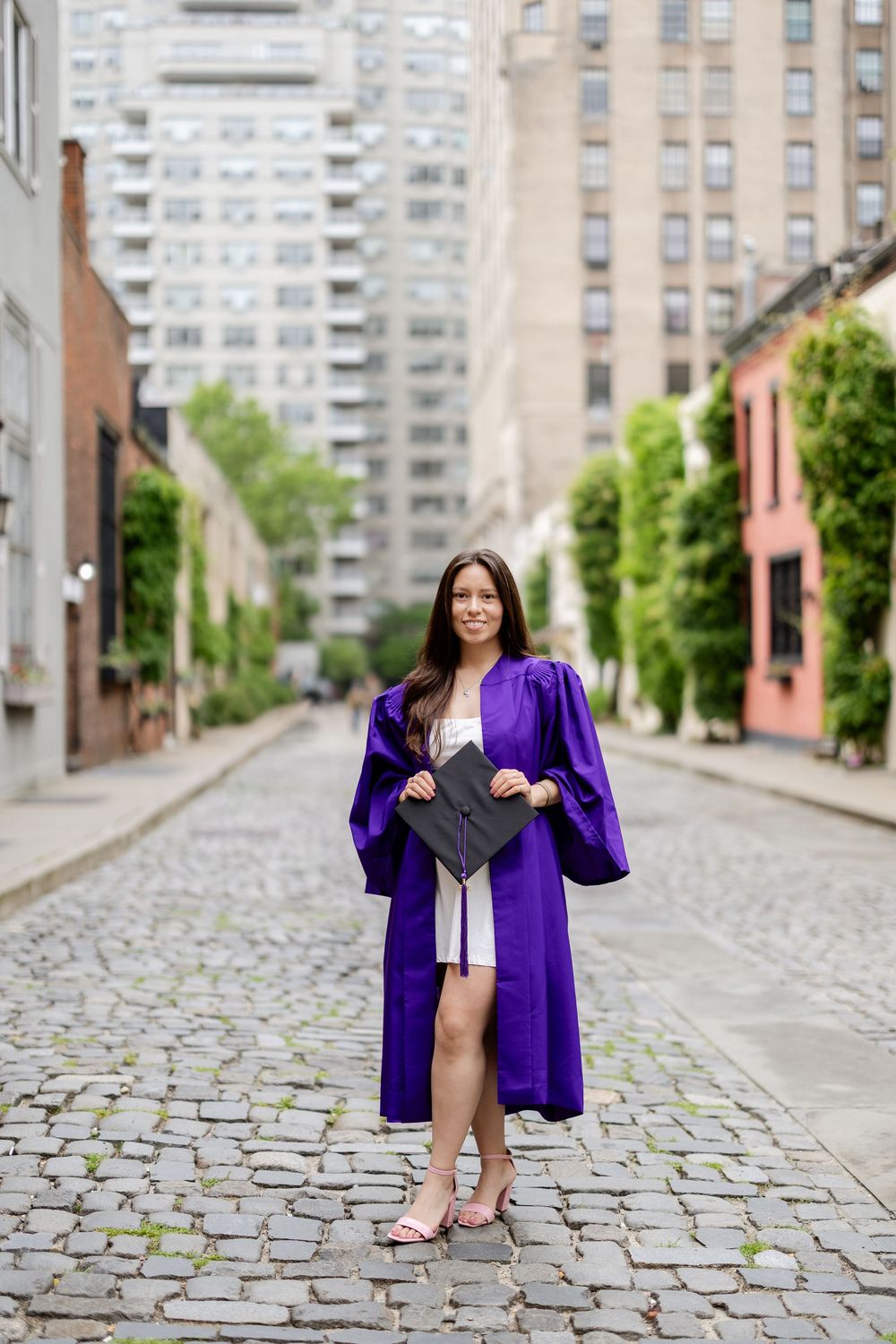 Graduation photos on a cobblestone street with city buildings in the background and someone in purple regalia posing.