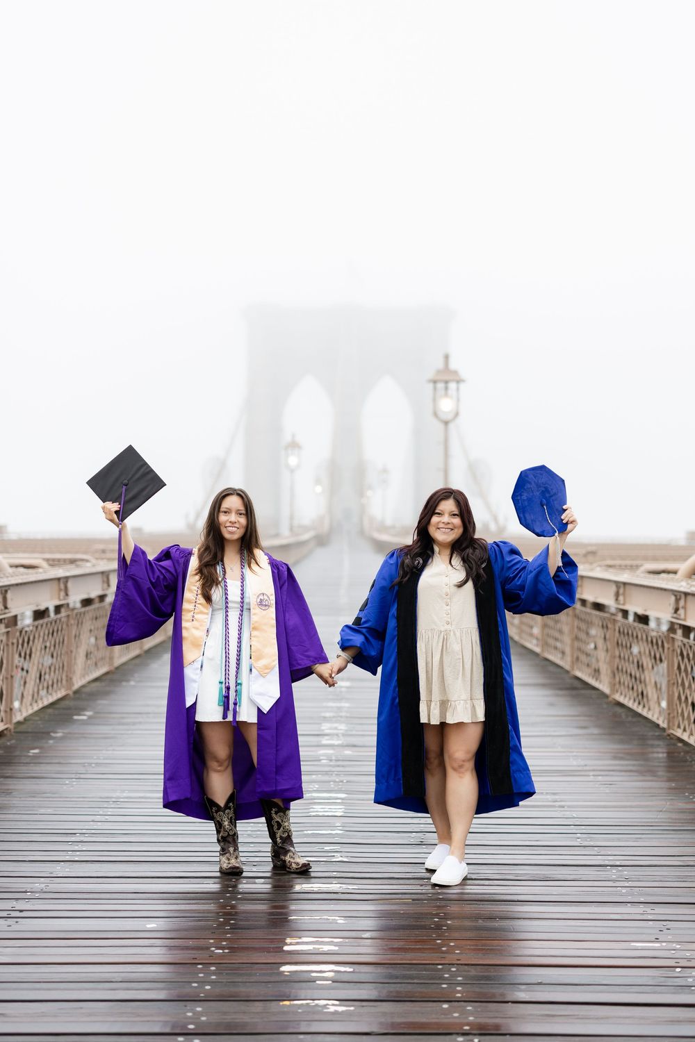 Two figures in bright blue and purple jackets standing on Brooklyn Bridge's wooden boardwalk.