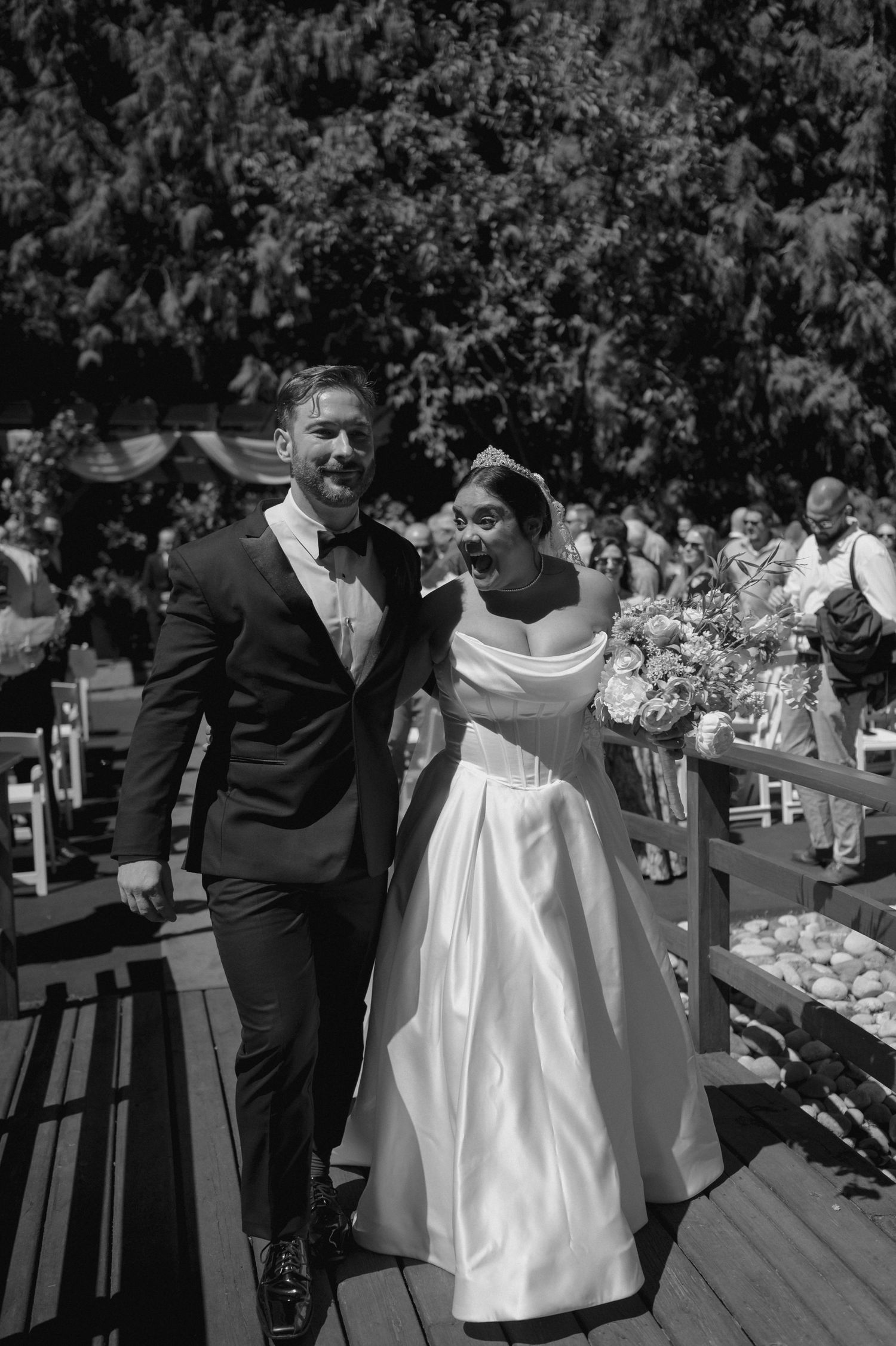 Black and white wedding photo of couple walking together on outdoor deck.