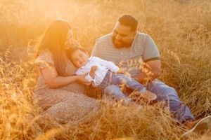Family relaxing together in golden field during sunset with warm backlighting.