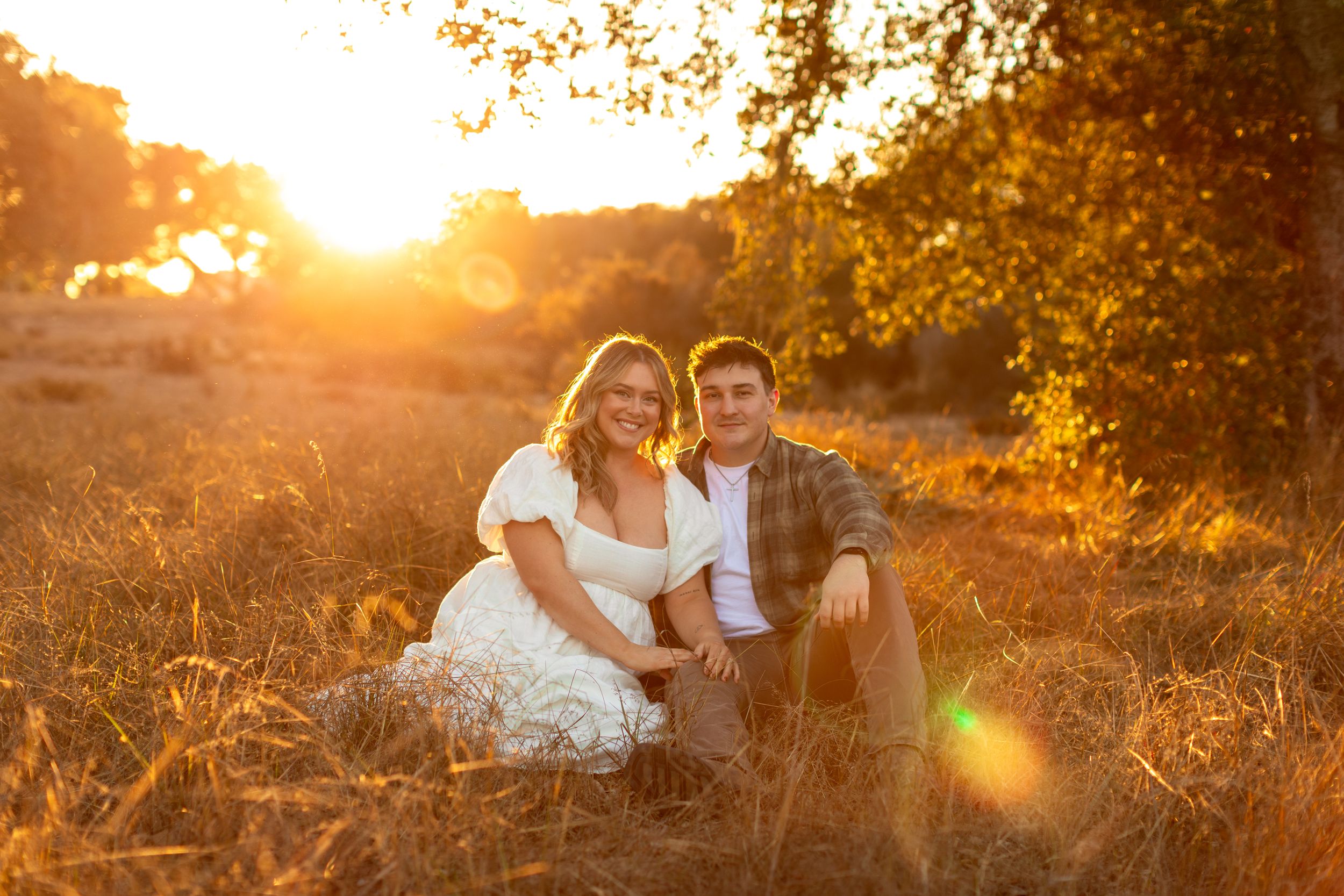 Couple sits together in field during golden sunset photography session.