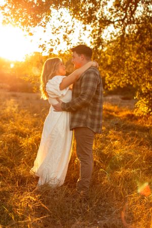 Romantic embrace between couple in white dress and plaid shirt during golden hour.