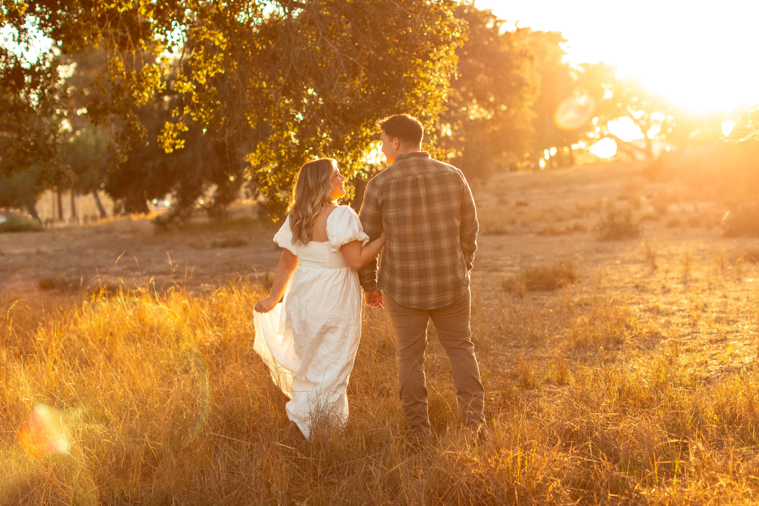 Couple walking hand in hand through golden field at sunset.