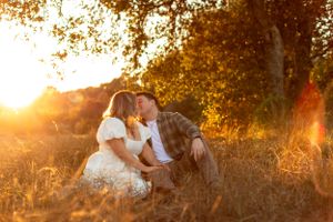 Intimate moment captured in a sunlit field with soft golden hour lighting filtering through autumn trees.