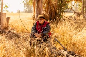 Person in red jacket sitting among tall dry grass during golden hour.
