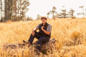 Person sitting on fallen log in golden field wearing casual attire during sunset.