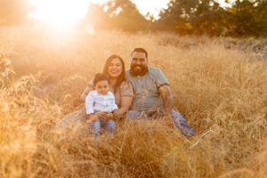 Family sitting together in tall grass field during sunset with warm golden lighting.