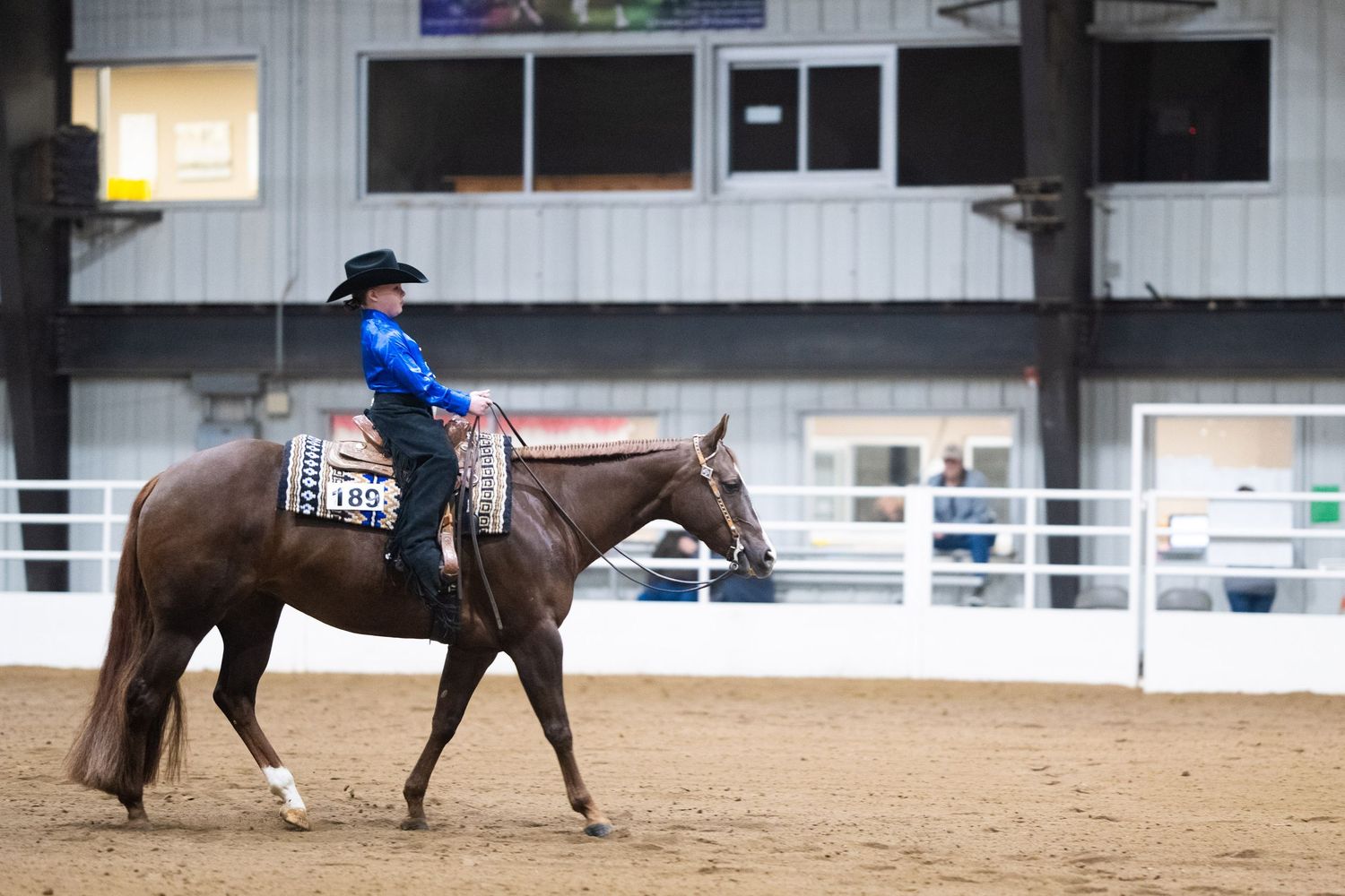 A rider on horseback performs a reining pattern in an indoor arena during a western riding competition.
