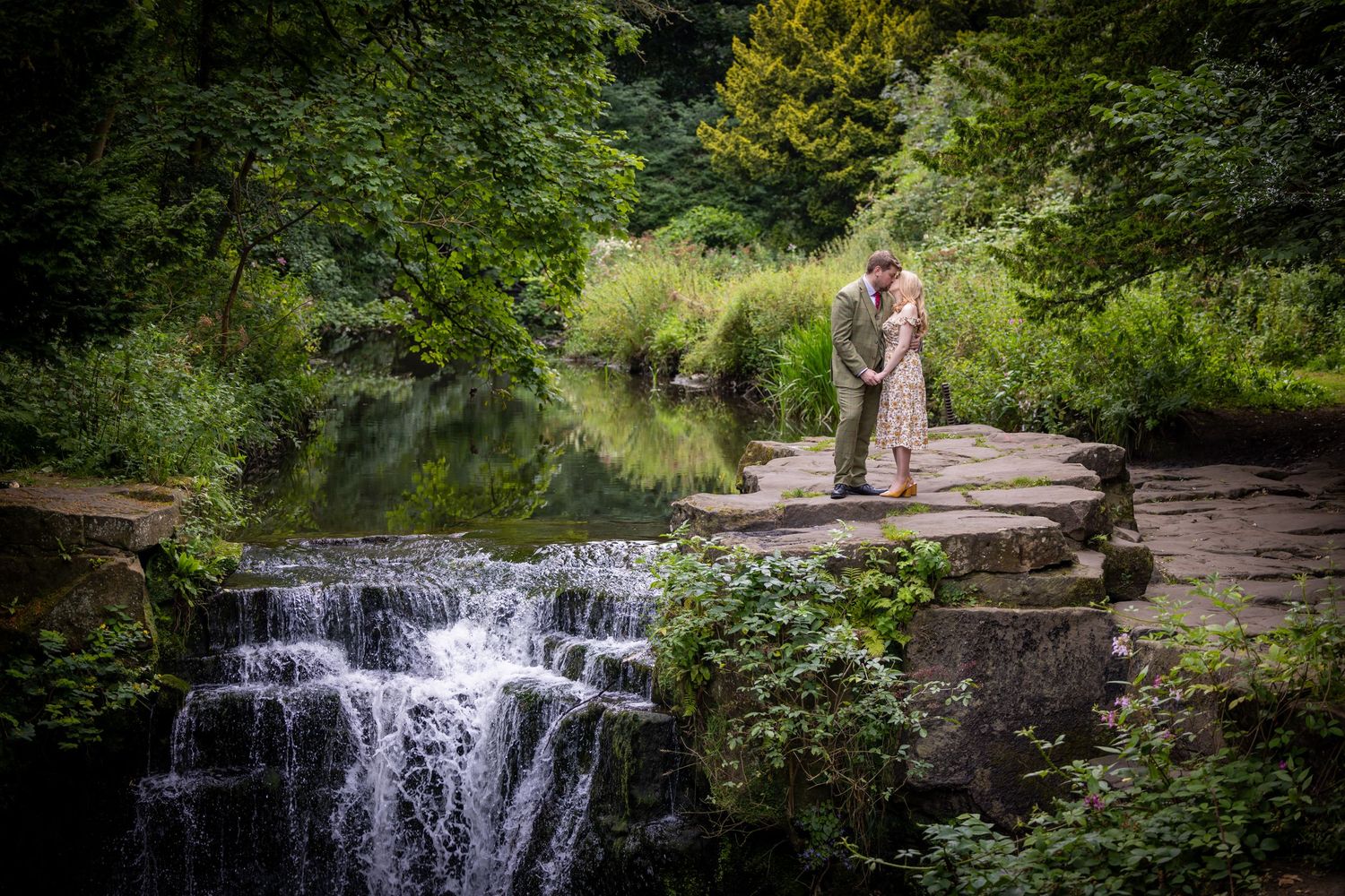 A cascading waterfall flows through lush green forest creating a peaceful natural scene in summer.
