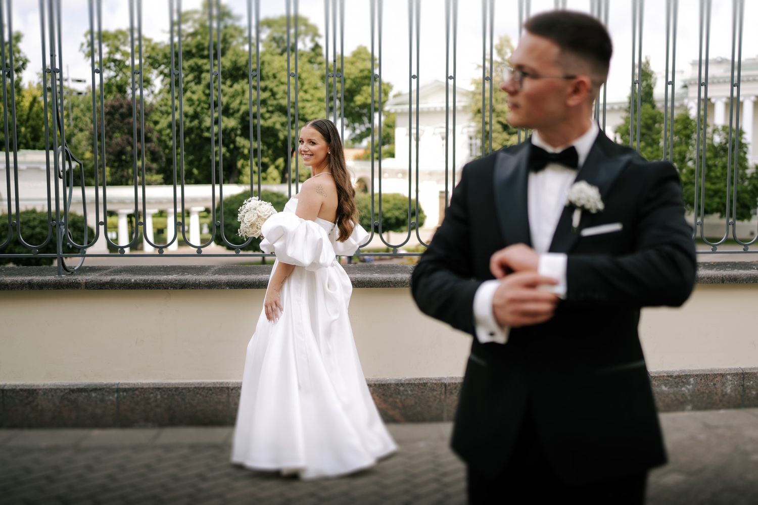 An elegant wedding portrait with the couple standing separately on a terrace with ornate railings.