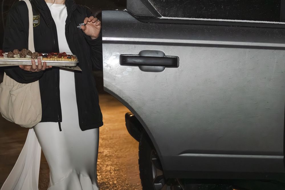 Dark nighttime photos of a bride carrying a leftover tray of desserts getting into a vehicle.