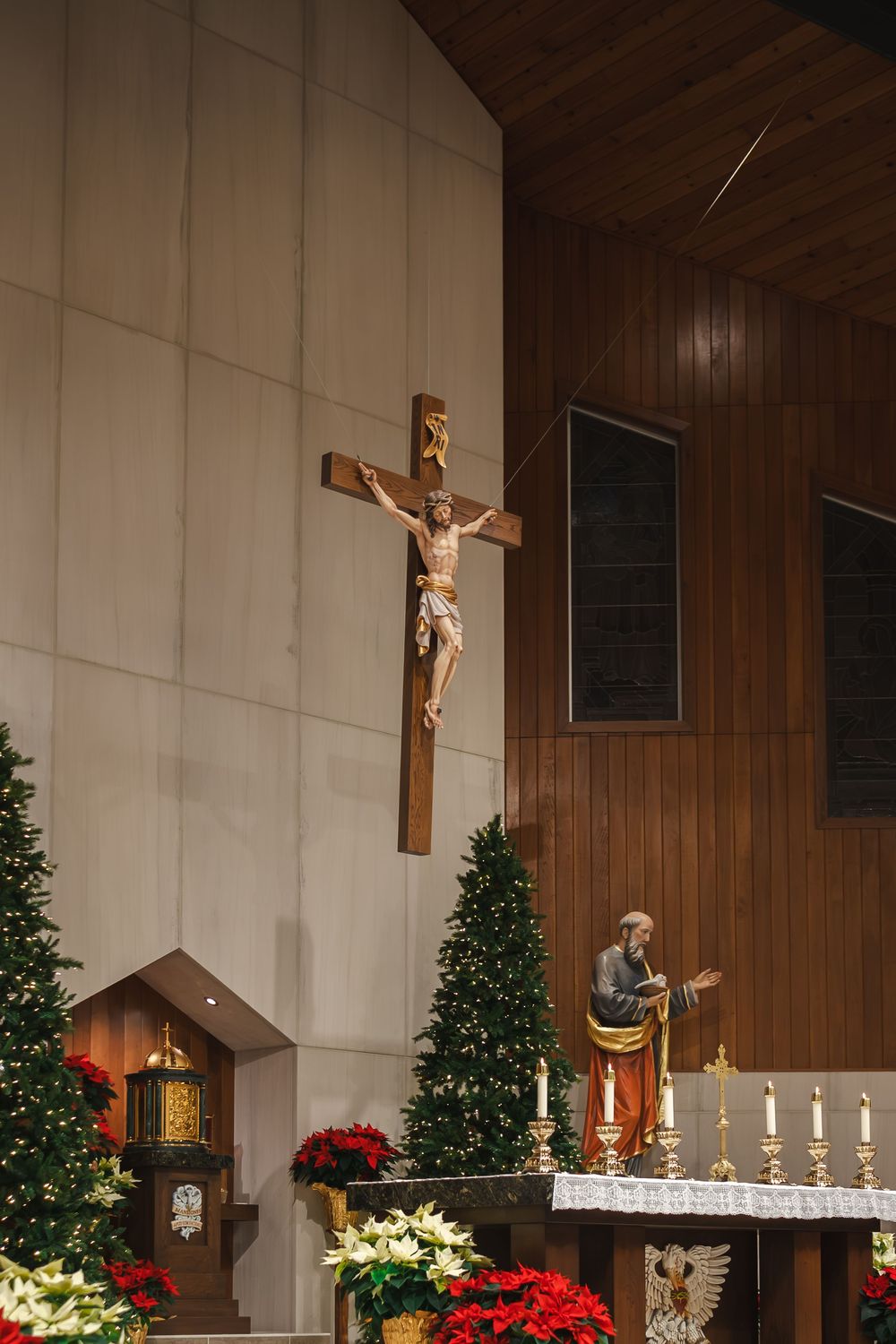 Church altar decorated for Christmas with crucifix, poinsettias, trees and candles.