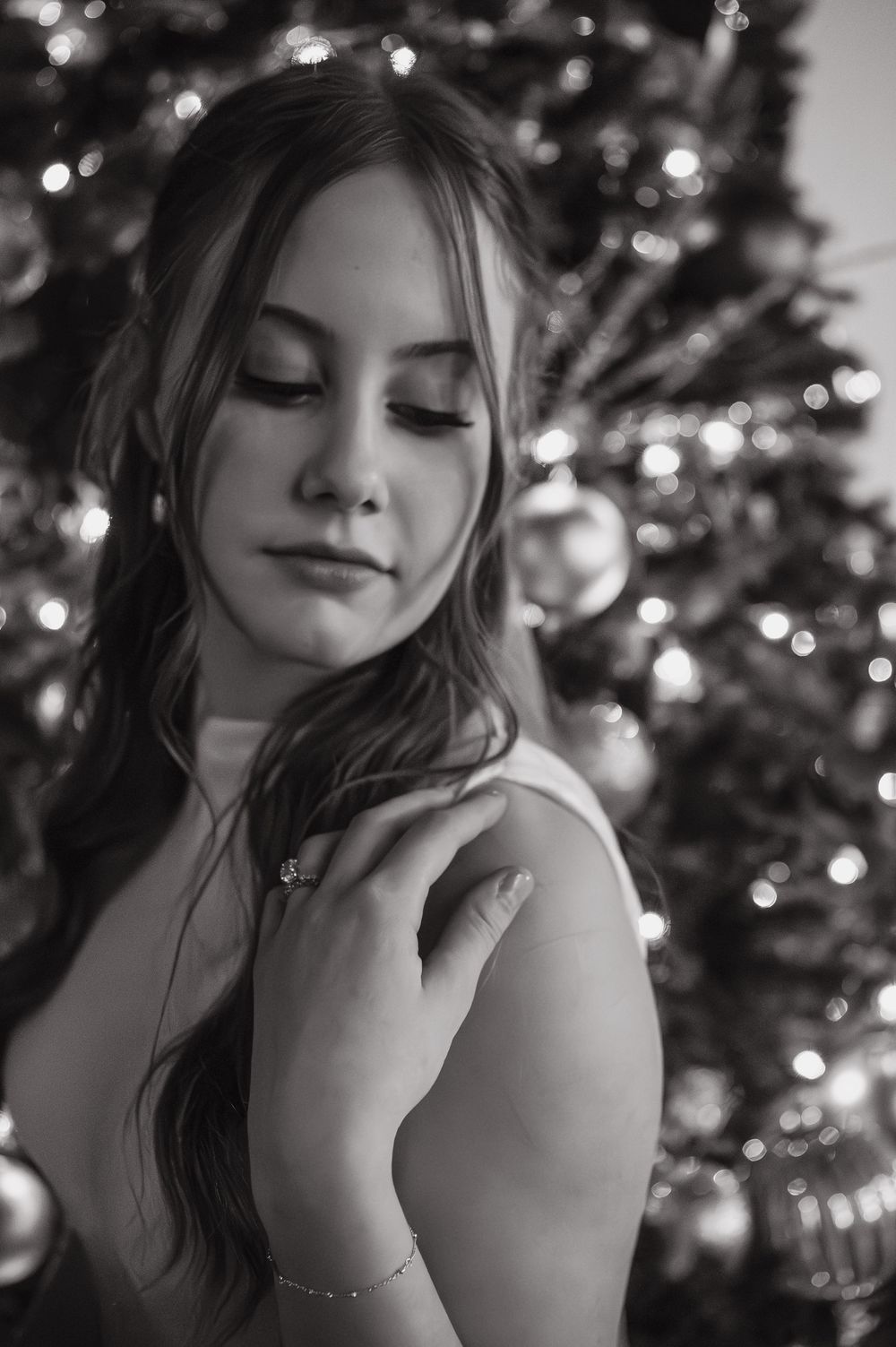 Artistic black and white portrait series with soft holiday lights and Christmas tree bokeh in background.