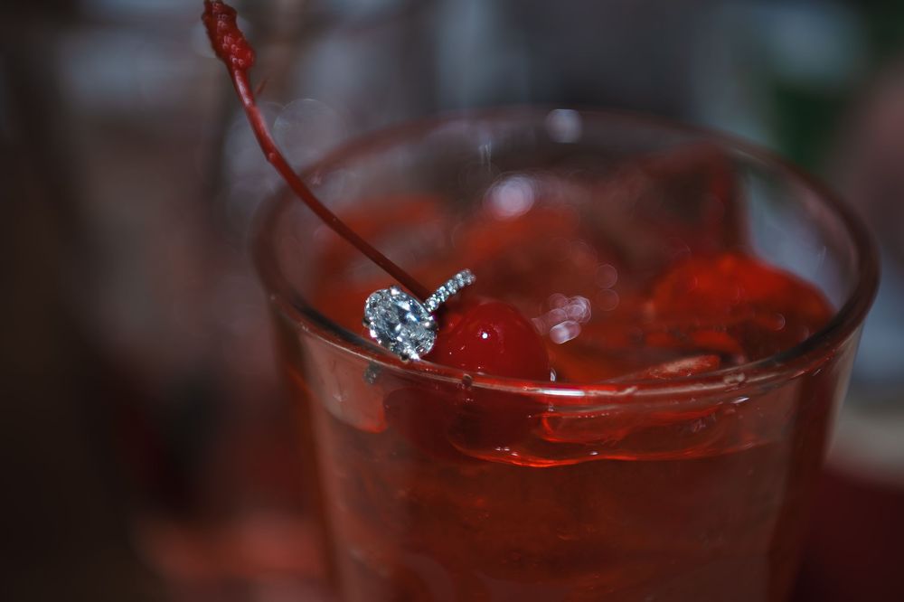 Close-up shot of a diamond ring around the stem of a maraschino cherry in a Shirley Temple drink.