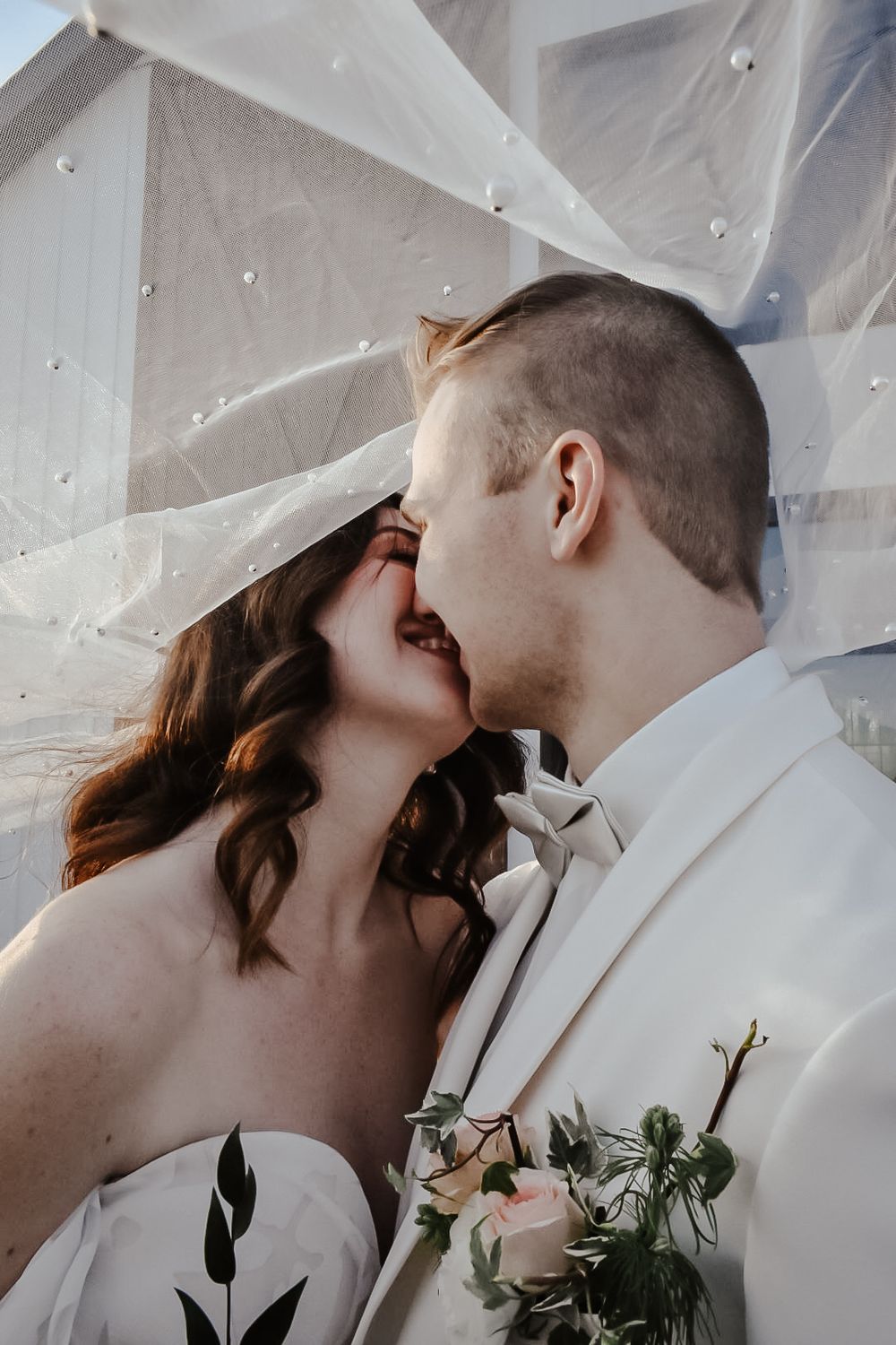 Romantic wedding couple sharing intimate moment under sheer fabric backdrop.