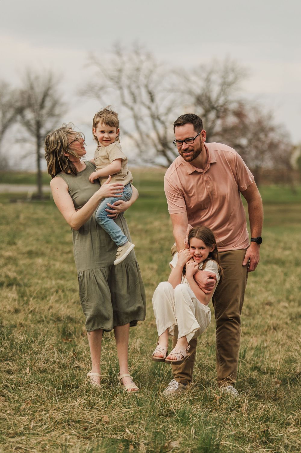 A family plays and laughs together while spending time outdoors in a grassy field on a cloudy day.