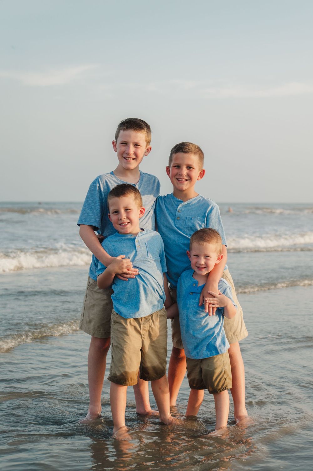 Family wearing matching blue shirts plays together in ocean waves at the beach during sunset.
