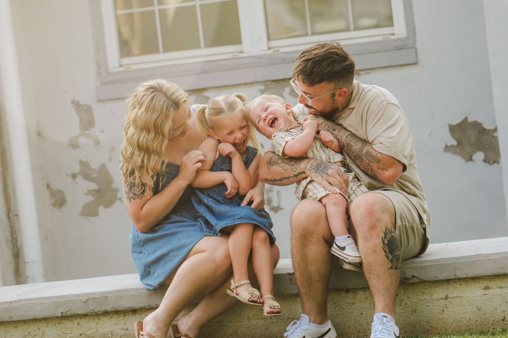 A family sits together on a white windowsill, sharing tender moments and embraces.