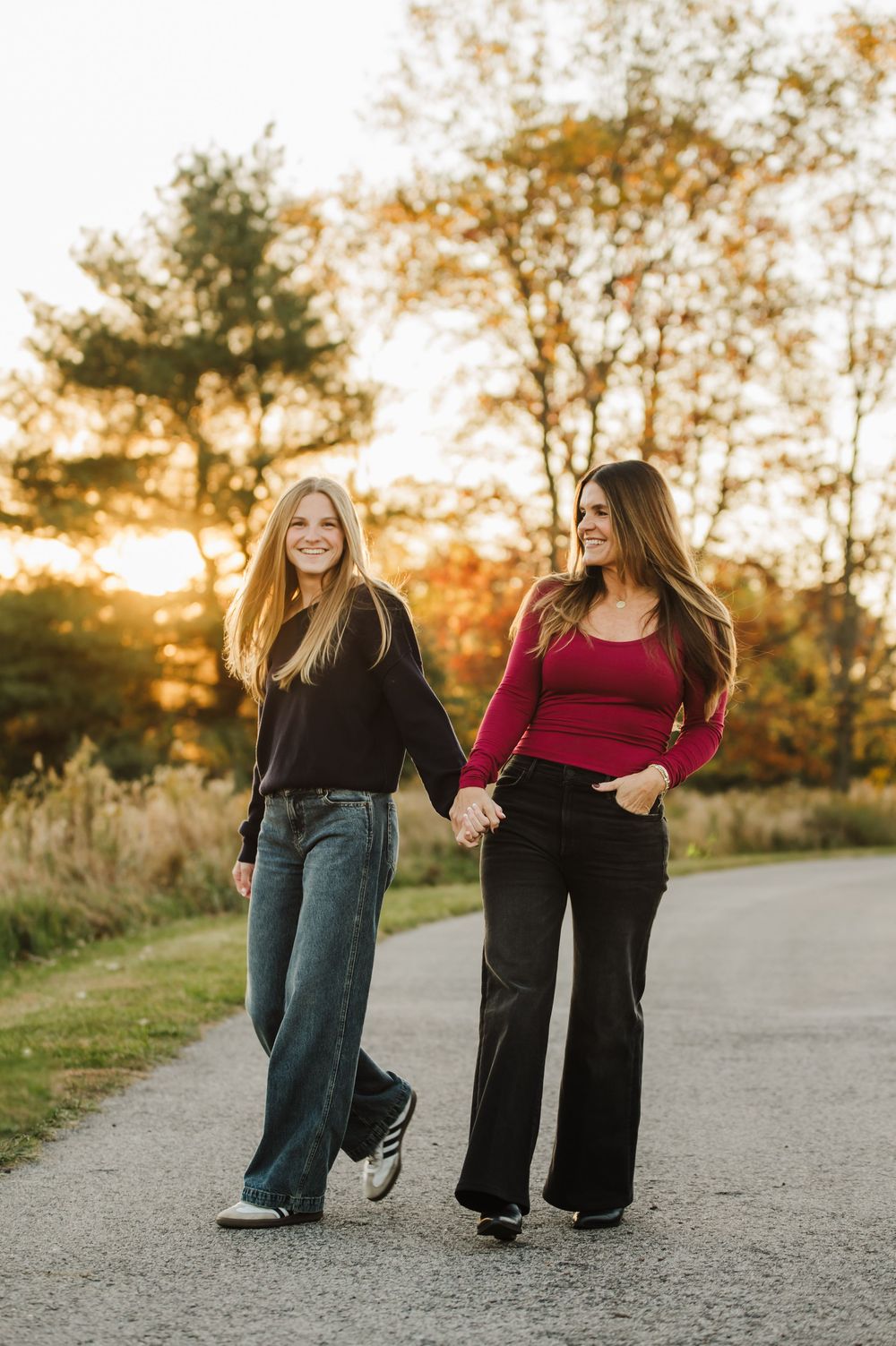 Two people walk together on a gravel path at sunset surrounded by autumn trees and golden light.