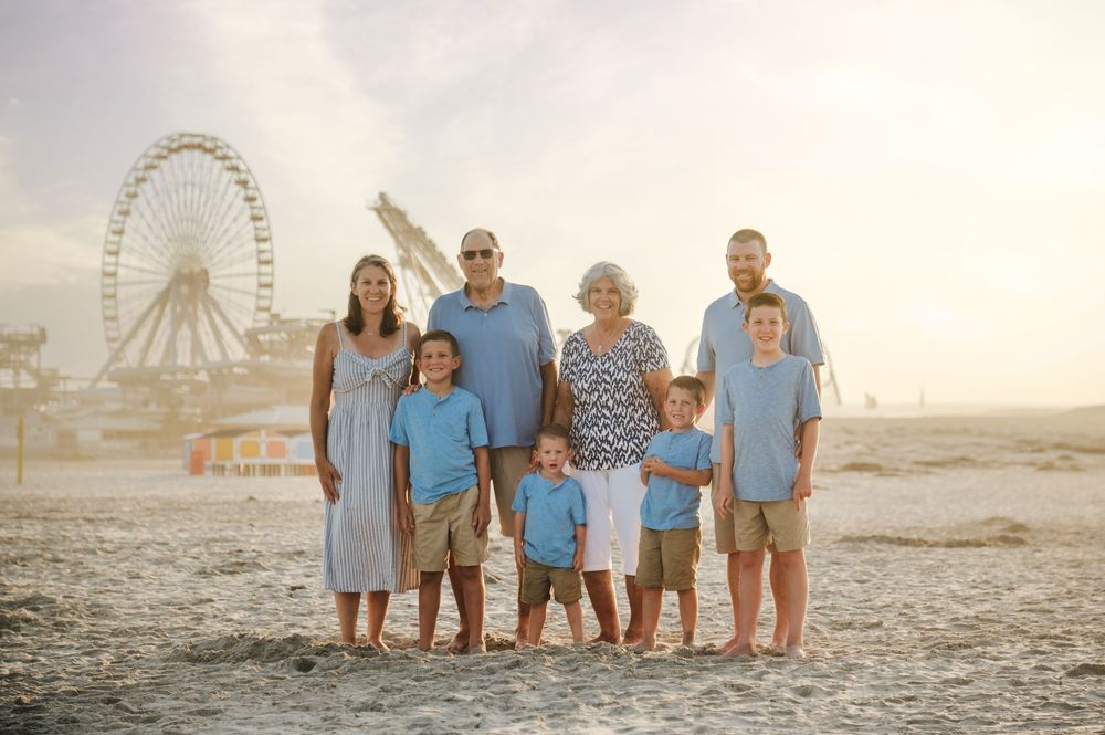A group poses for photos at sunset on a beach with a Ferris wheel visible in the background.