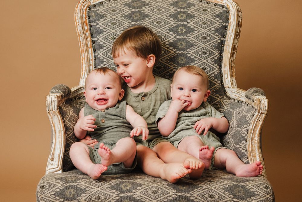 A series of connected photos showing two babies in matching outfits sitting together on an antique patterned chair.