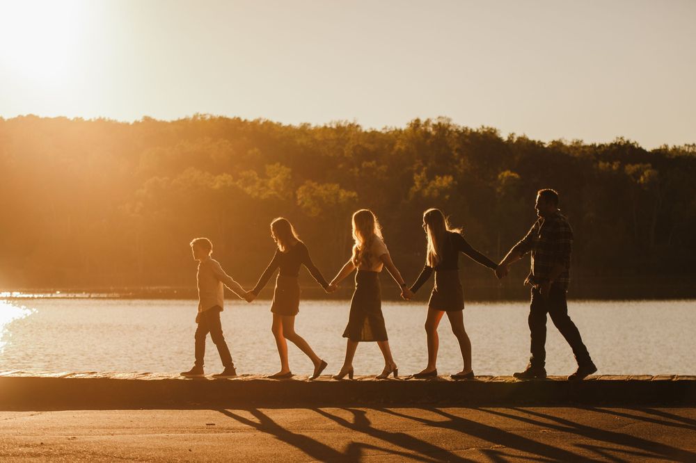 Silhouettes of people holding hands walking in a line along a beach at sunset, creating a peaceful scene.