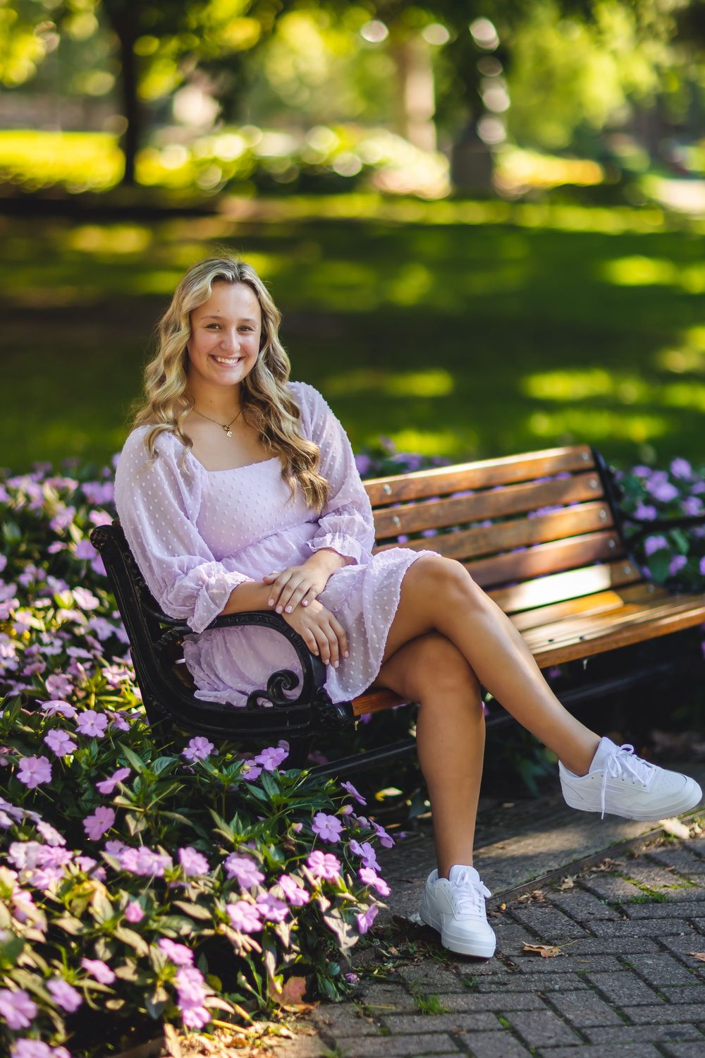 Senior portrait on wooden bench with pink flowers and bokeh lighting in background.