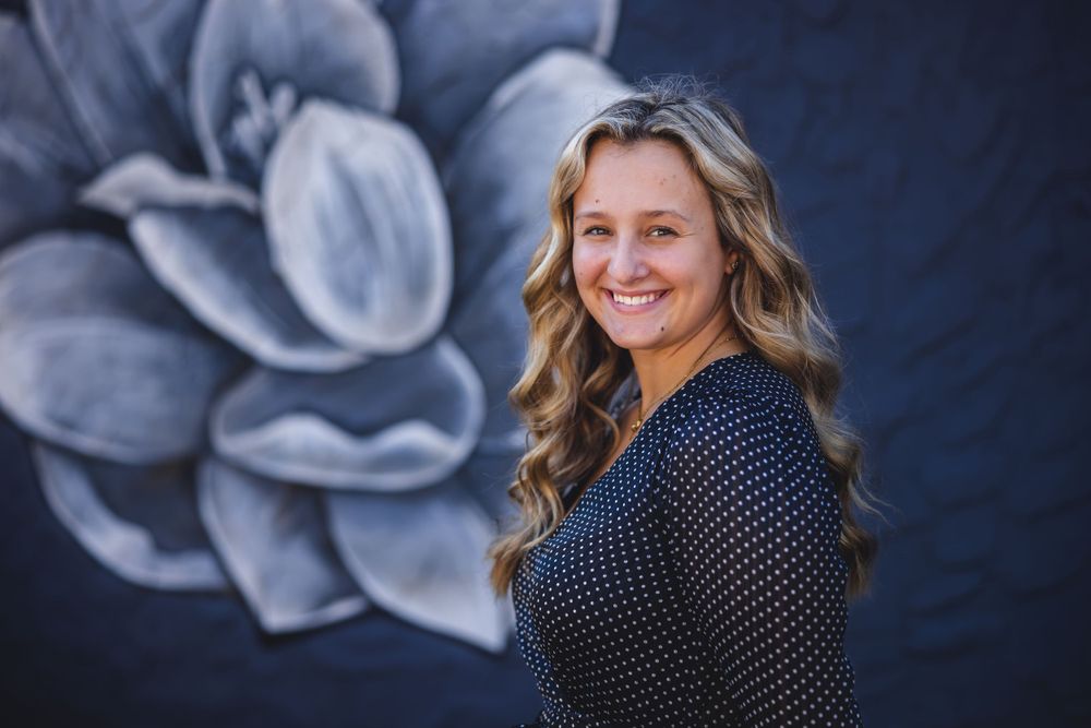 Portrait against blue and gray floral mural wall in polka dot dress.