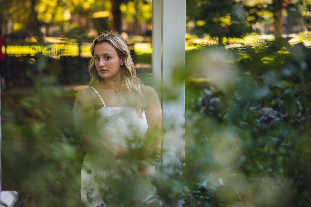 Artistic portrait through foliage wearing white dress with dreamy lighting.