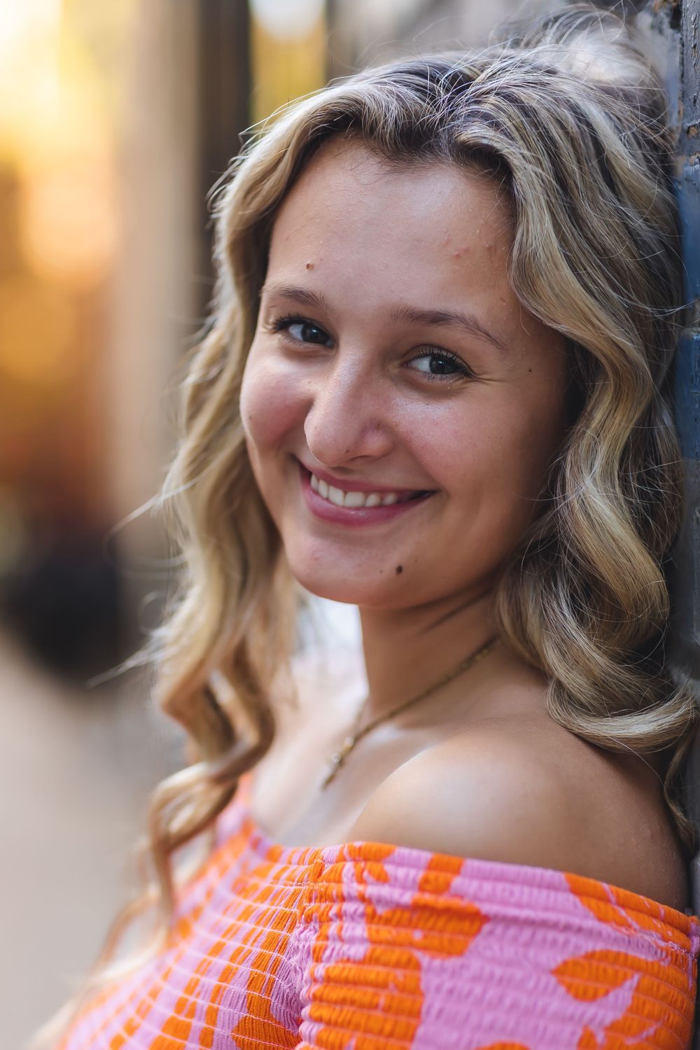Close up portrait of person in orange off-shoulder dress with wavy hair and natural makeup.