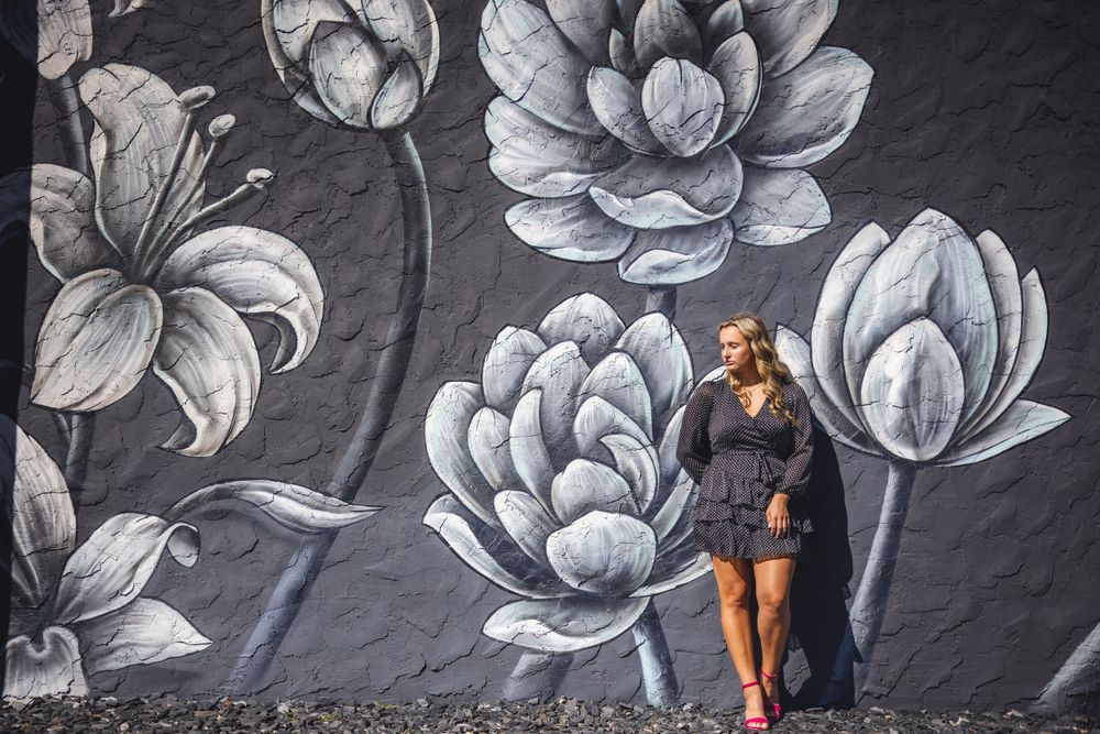 Fashionable portrait against large floral wall mural in black polka dot dress.