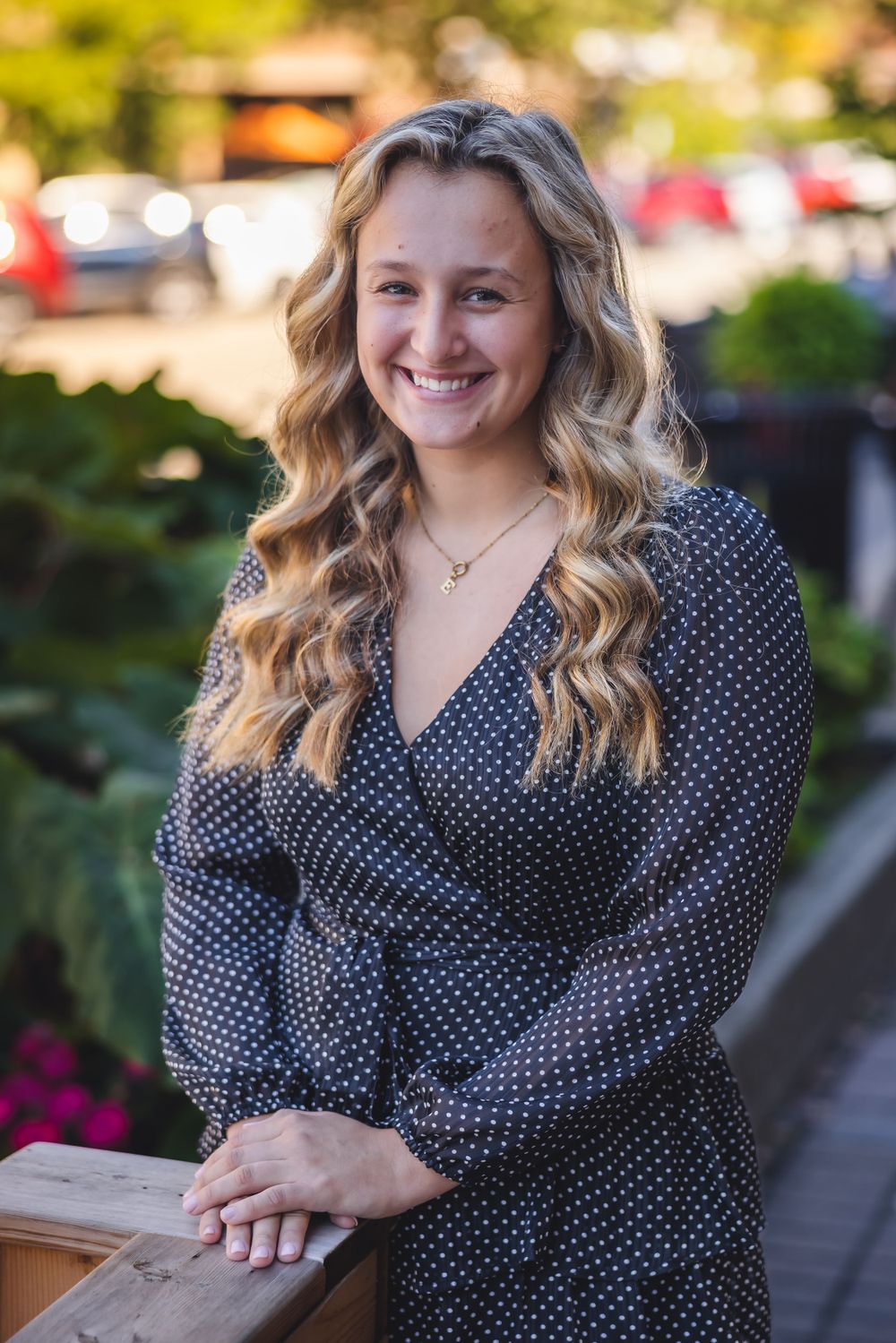 Woman in polka dot dress smiles outdoors with wavy blonde hair.