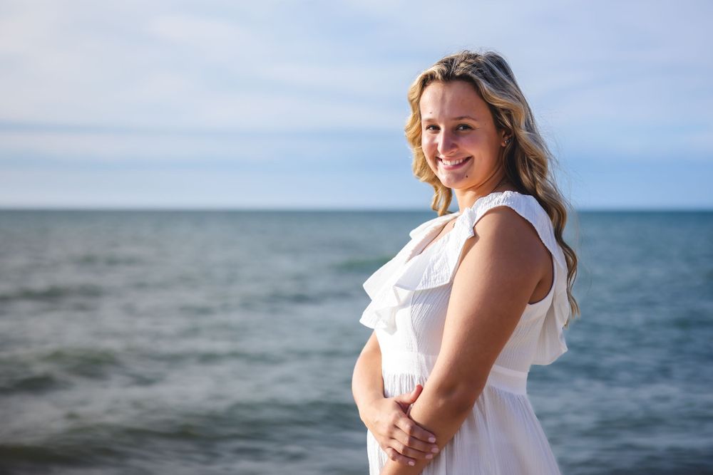 Beachside portrait in white dress with ocean waves and blue sky in background.