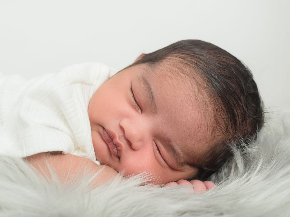 A peaceful newborn boy sleeping on a soft white fur, captured in a photo by Abigail's studio in High Wycombe.