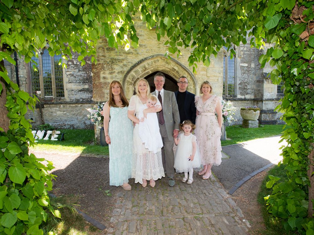 A family poses for a photo in front of a church, captured during a christening by Abigail's studio in High Wycombe.