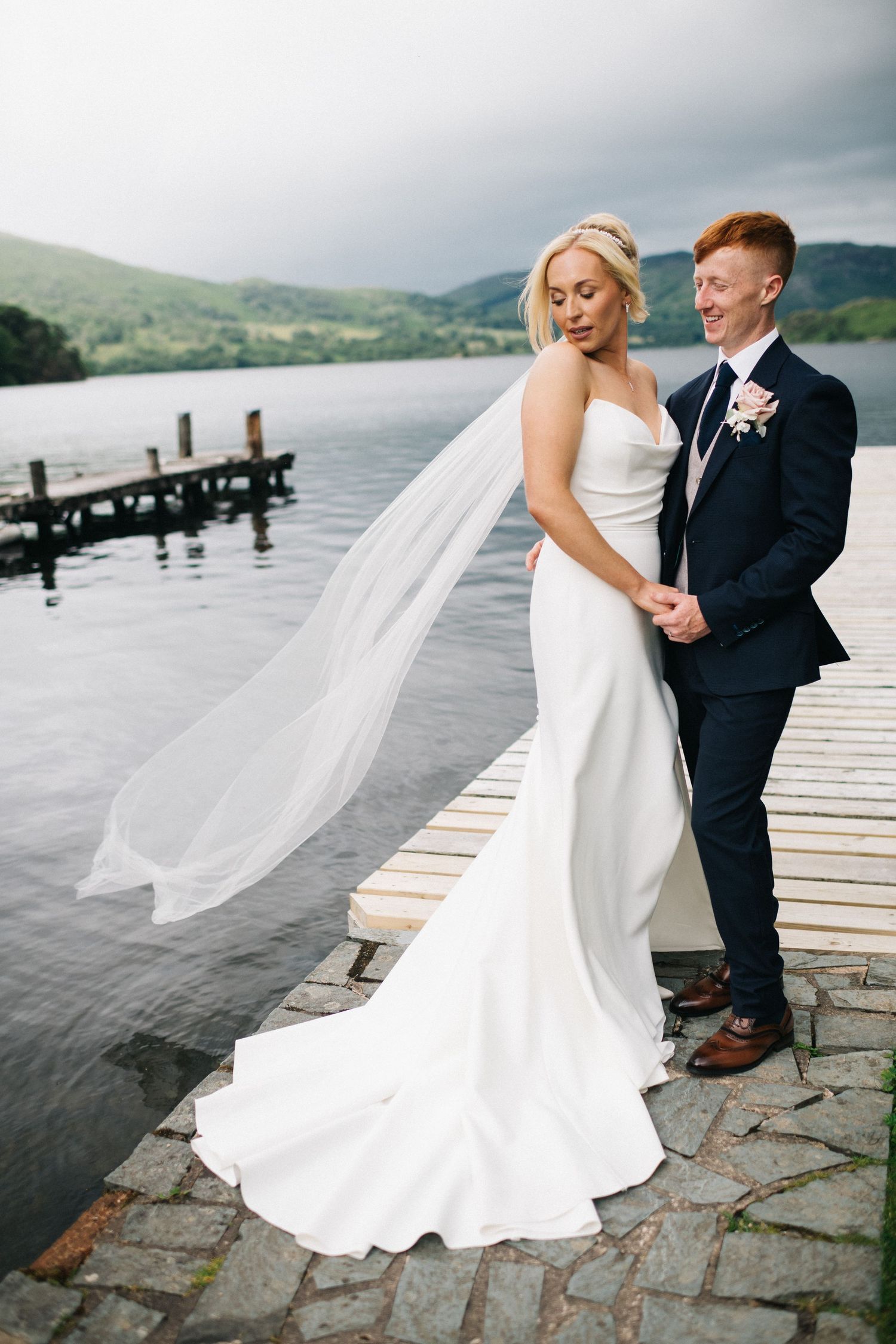 A romantic wedding couple dances together on a lakeside dock with mountains and moody skies in the background at the Inn on the Lake.