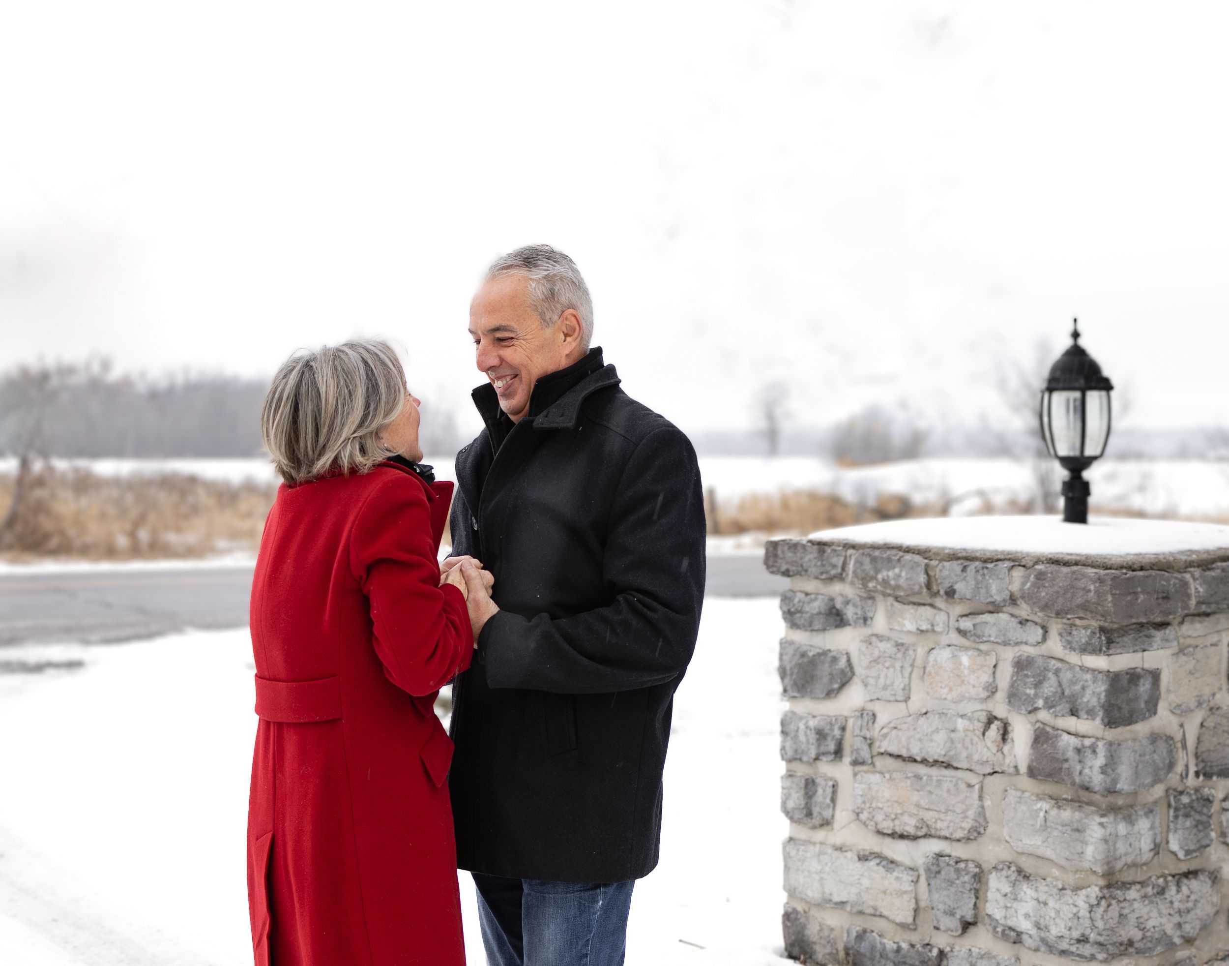 Romantic winter photoshoot of a couple by a stone wall in a snowy setting.