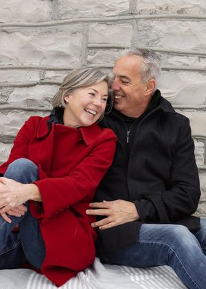 Couple in red and black coats sharing intimate moments against a stone wall backdrop.