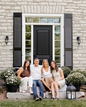 Family group sitting casually on steps of a white stone house with black shutters.