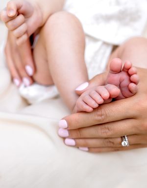 Close-up of tiny baby feet being gently held by manicured hands with a sparkling ring.
