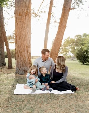 A casual outdoor family portrait taken under tall pine trees on a blanket.