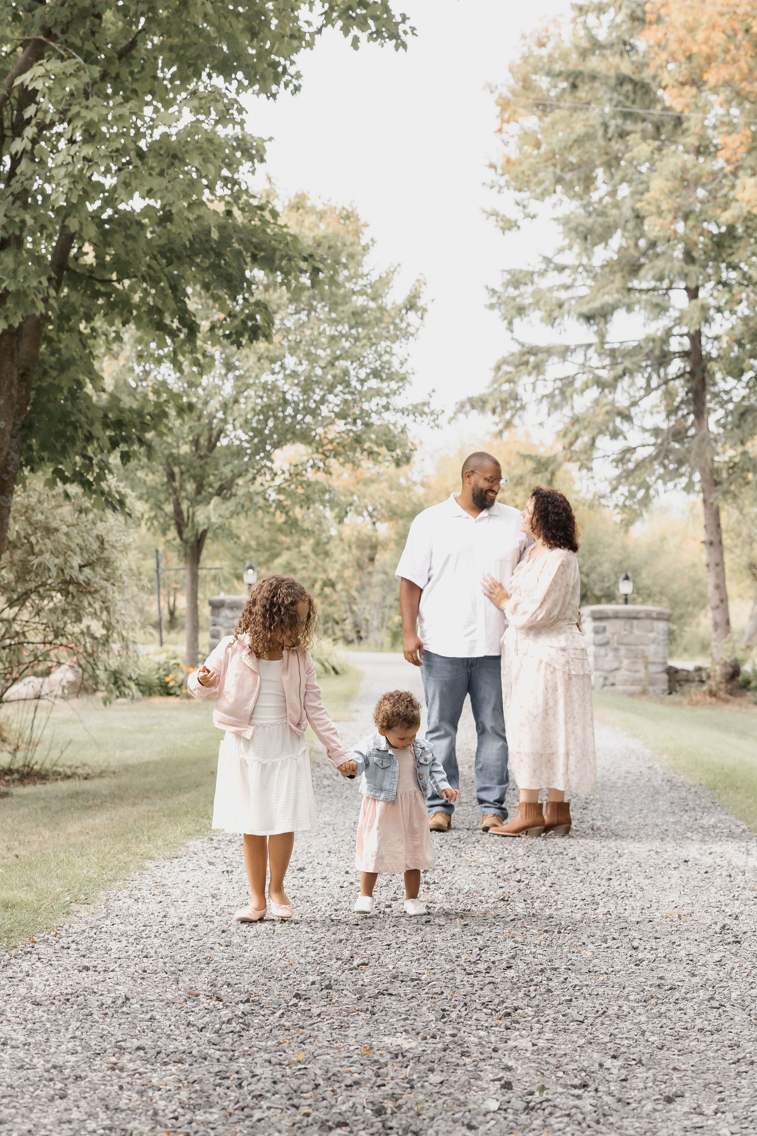 A family walks together on a gravel path surrounded by lush trees and landscaping.