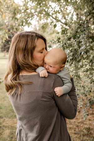 A tender moment between parent and baby captured outdoors among leafy greenery.
