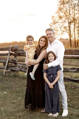 A sunset family portrait taken against a rustic wooden fence in warm golden light.