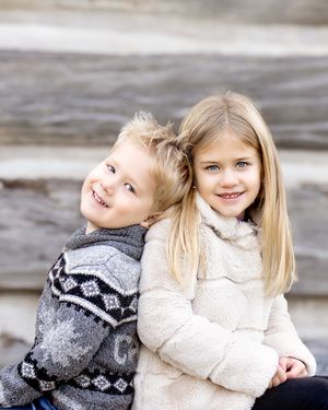 Two children in winter sweaters laughing and playing together during a photo session.