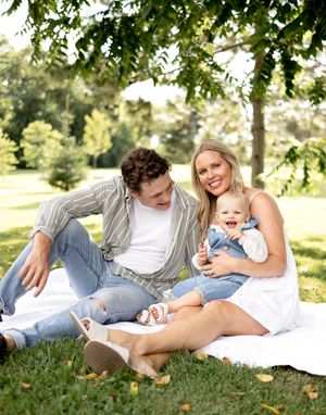 A relaxed family picnic scene on a white blanket with a dog in a sunny park.